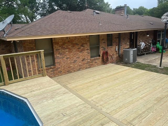 Backyard deck with a brick house, small pool, and wooden railing under an overcast sky