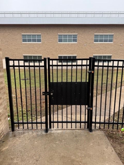 Black metal gate and fence blocking a concrete path in front of a brick building.