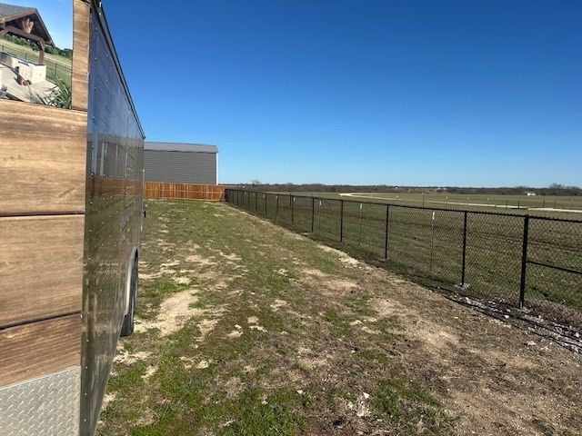 Fence-lined dirt path beside a building under a clear blue sky