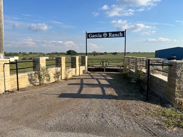 Entrance gate to Garcia Ranch with stone walls and a gravel drive under a blue sky