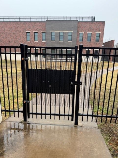 Black metal gate in front of a brick building on a wet sidewalk.