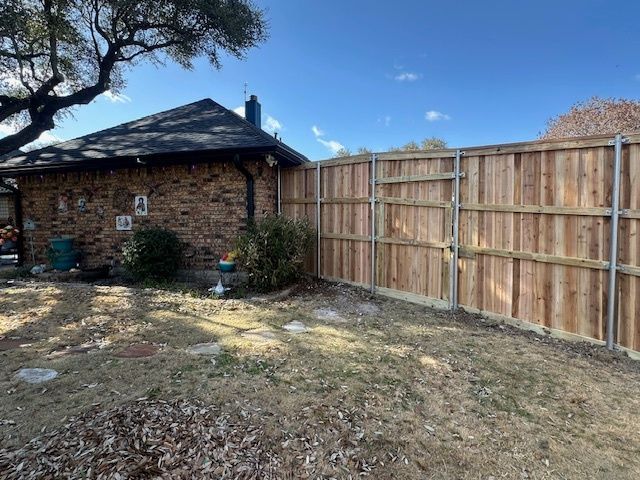 Backyard with brick house, wooden fence, and sparse grass under a blue sky