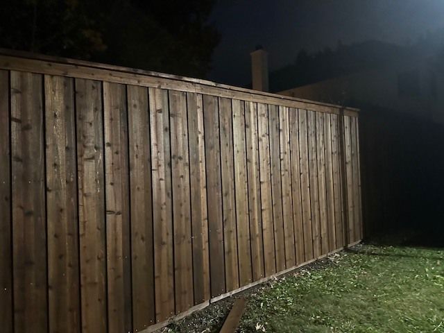 Wooden privacy fence along a grassy yard at night, lit by outdoor lights.