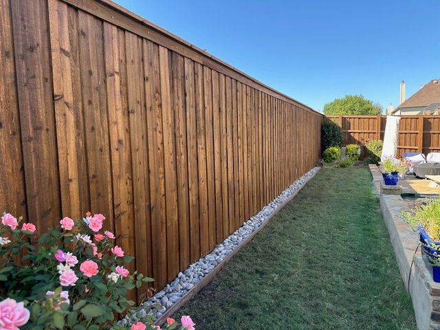 Long wooden fence beside a narrow grassy yard with pink flowers in the foreground