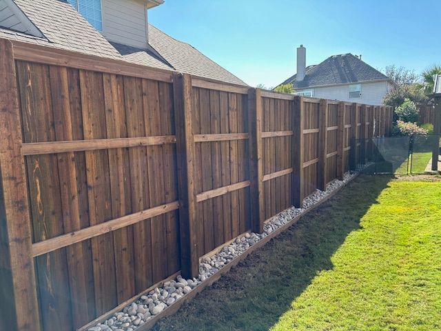Long wooden fence along a grassy backyard with gravel edging and neighboring houses in the background