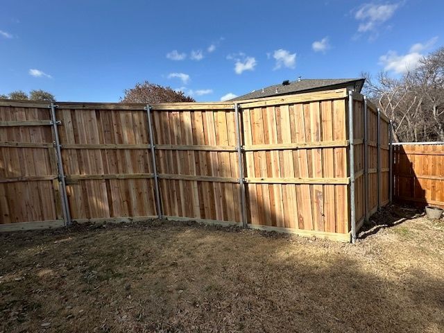 Wooden backyard fence with a gate under a blue sky on a grassy lawn