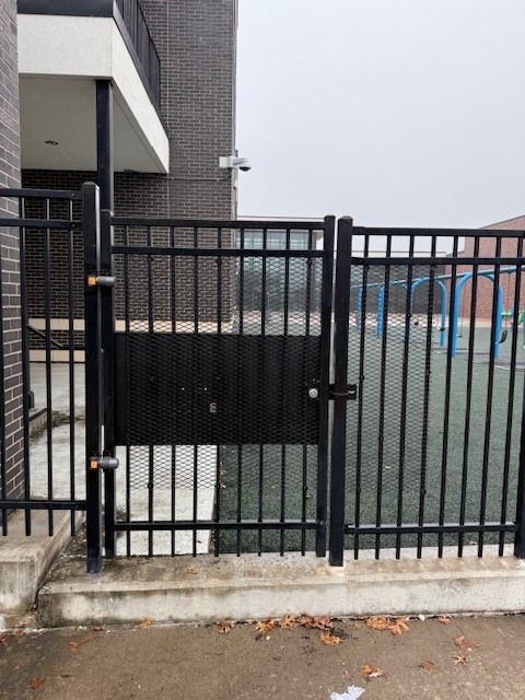 Black metal fence and gate in front of a building entrance, with a sidewalk and fallen leaves.