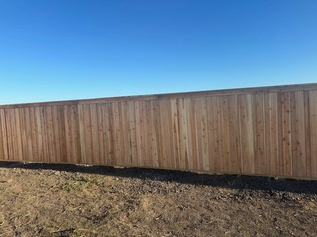 Wooden fence along a dry grassy yard under a clear blue sky