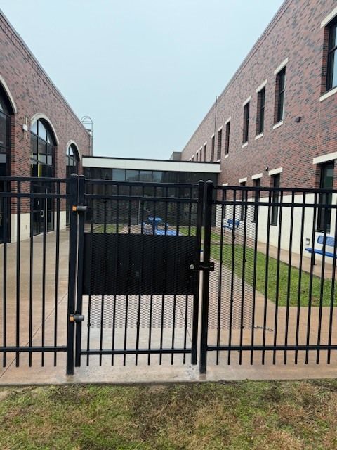Black metal gate between two brick buildings, blocking a narrow courtyard walkway.