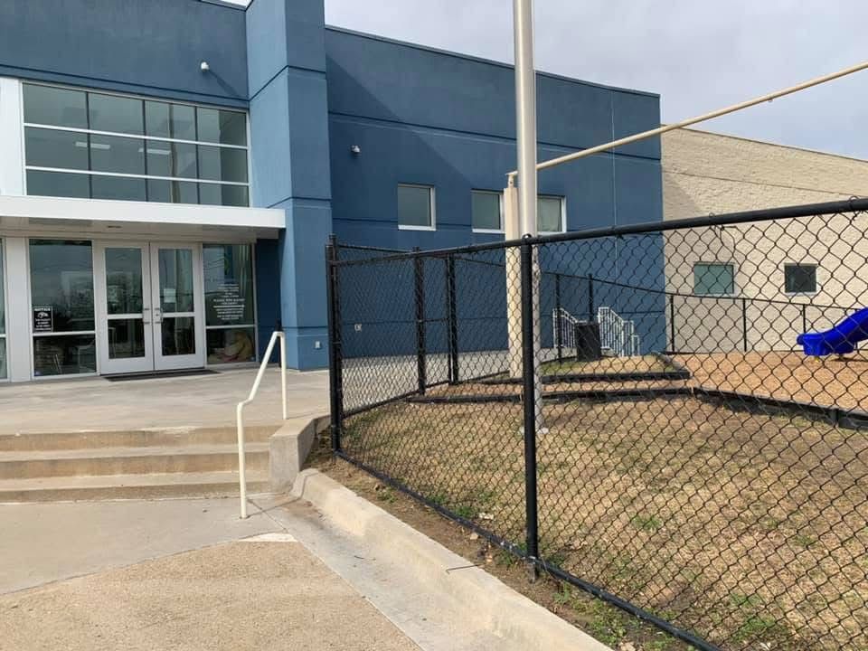 School building entrance with steps, ramp, chain-link fence, and blue playground slide