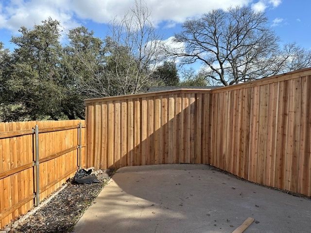 Wooden-fenced concrete patio with curved corner, under blue sky with trees beyond the fence