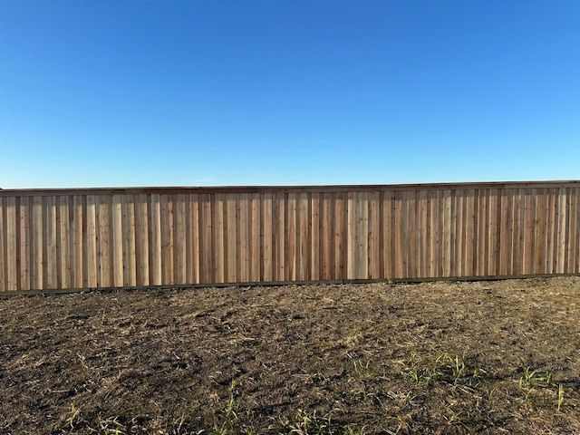 Wooden fence behind a bare, uneven dirt yard under a clear blue sky.