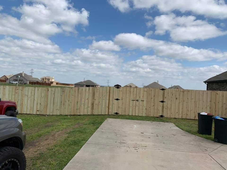 Backyard with concrete driveway, wooden fence, cloudy sky, and trash bins on the right