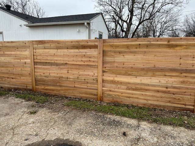 Wooden privacy fence along a gravel driveway beside a white building on an overcast day