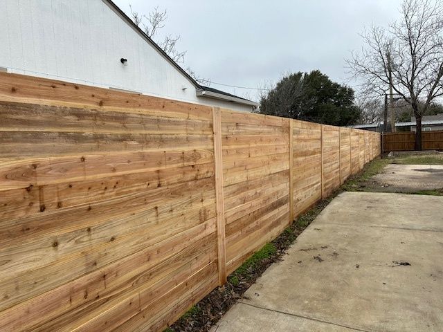 New wooden privacy fence along a concrete driveway beside a white house