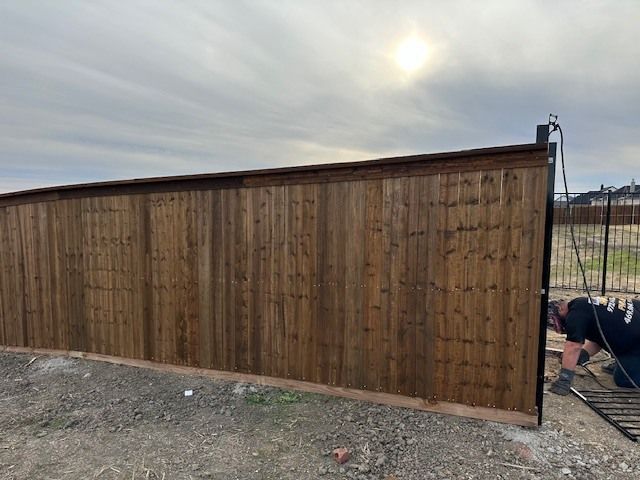Long wooden privacy fence under a cloudy sky, with a worker near the right end.