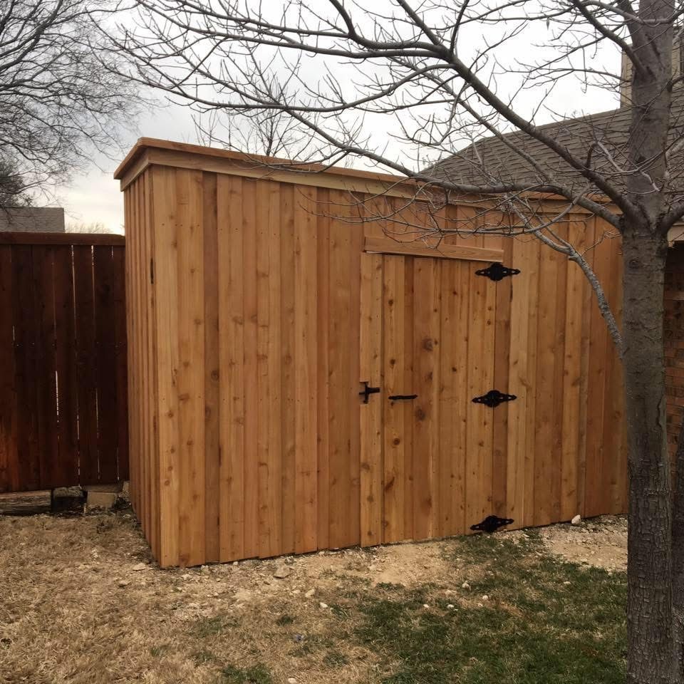 Wooden backyard storage shed with double doors, beside a fence and leafless trees.