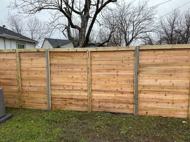 Wooden privacy fence in a backyard with trees and a grassy lawn