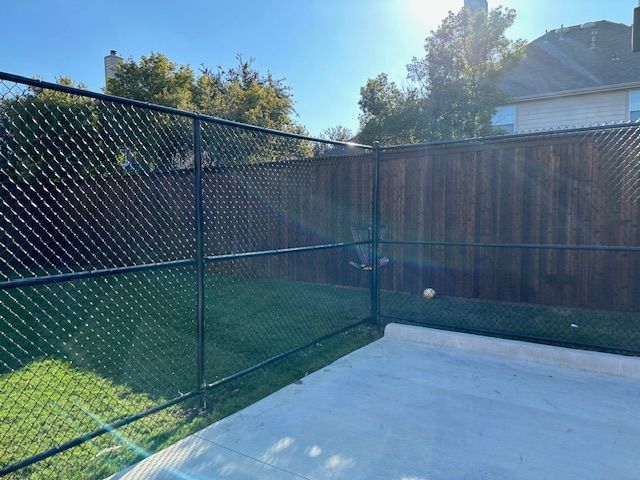 Chain-link fence beside a concrete patio and wooden privacy fence in a sunny backyard