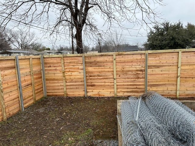 Wooden backyard fence enclosing bare ground with stacked wire mesh in the foreground