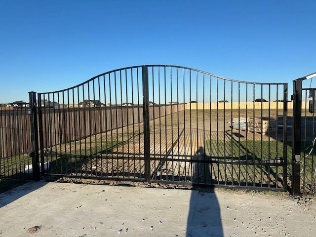 Black metal gate with vertical bars across a driveway entrance under a clear blue sky