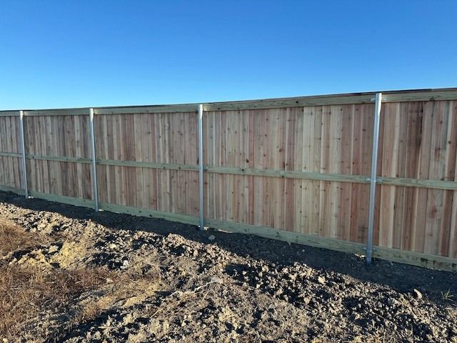 Wooden privacy fence along a dirt lot under a clear blue sky.