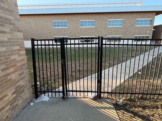 Black metal gate blocking a sidewalk entrance beside a brick building and grassy courtyard
