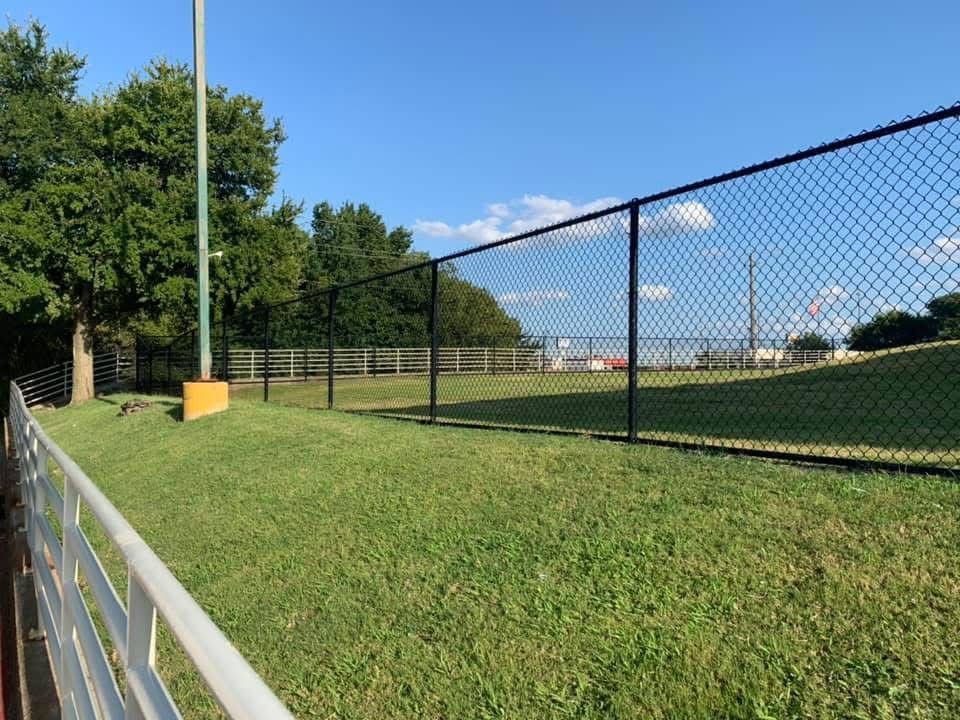 Chain-link fence along a grassy park path with trees and a blue sky.