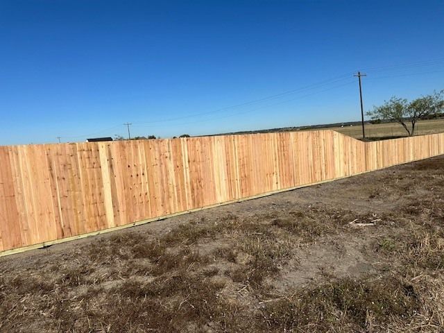A long wooden fence along a dry, brown field under a clear blue sky.