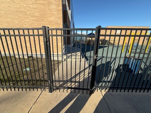 Black metal fence gate blocking a concrete walkway between brick buildings in bright sunlight