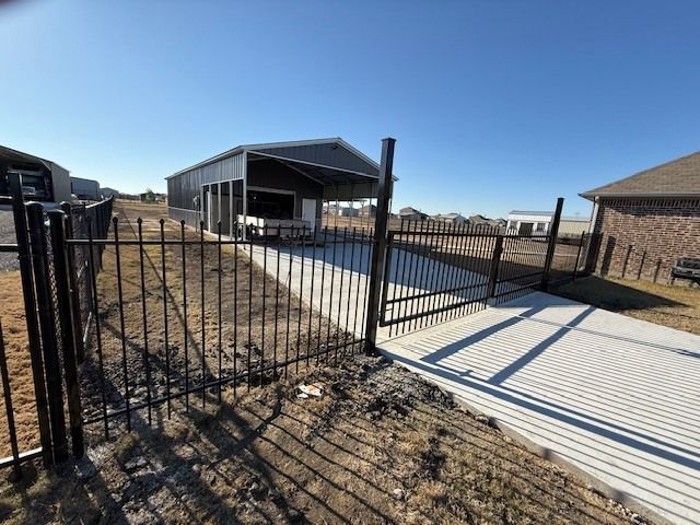 Black metal fence beside a concrete driveway and modern house under a clear blue sky