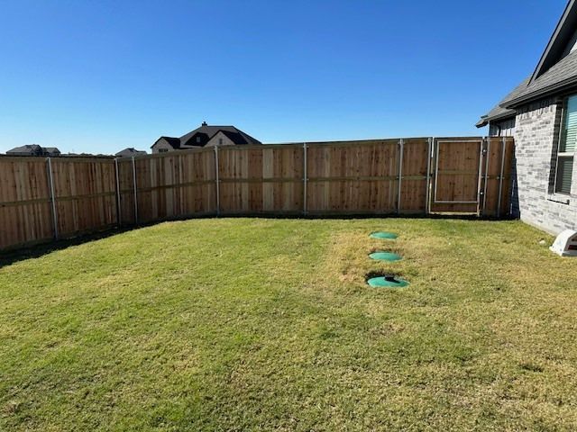Backyard with green lawn, wooden fence, and a house exterior under a clear blue sky