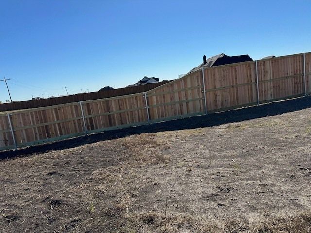 Empty dirt lot with a wooden fence under a clear blue sky