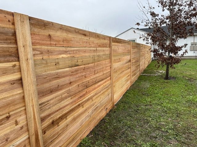 New wooden privacy fence along a grassy yard with a tree and house in the background