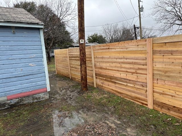 Backyard with blue shed, wooden fence, muddy ground, and utility pole under cloudy sky