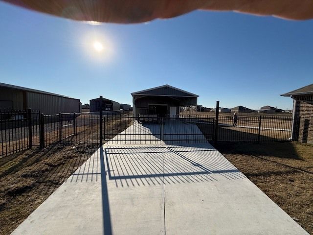 Gated concrete walkway leading to a small building under bright sun in a dry landscape