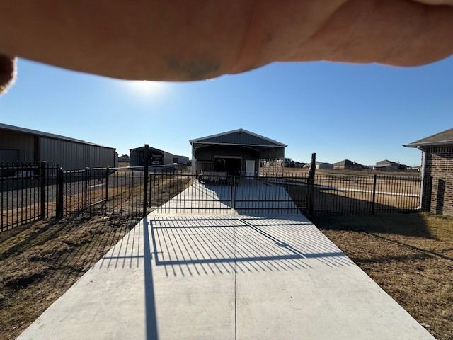 Driveway leading to a gated house with black fences under a clear blue sky.