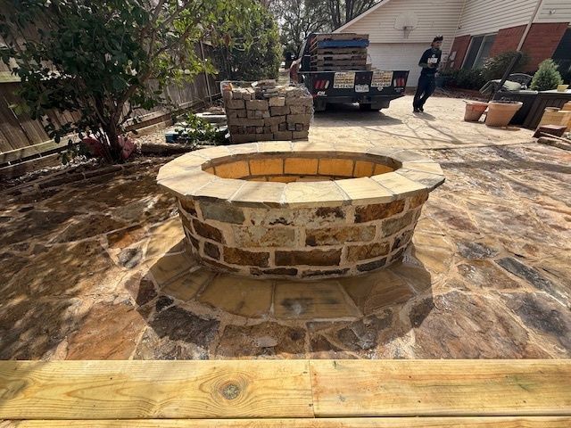 Stone fire pit in a sunlit backyard patio with a truck and person in the background