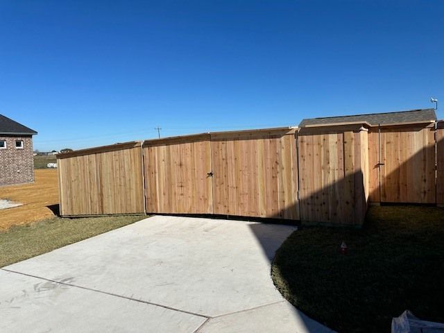 Wooden privacy fence along a concrete driveway beside a house, with sun and shadow.