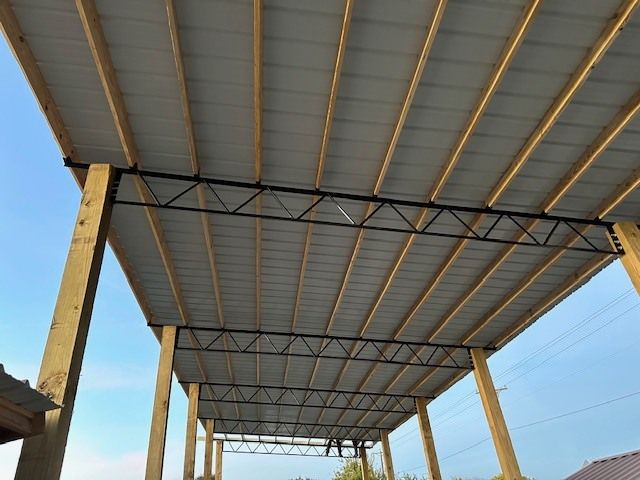 Metal-roofed open structure with wooden support posts against a blue sky