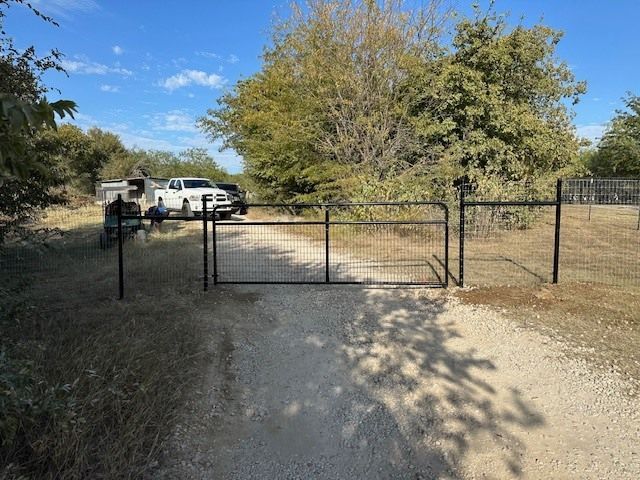 Gravel driveway with a metal gate, white pickup truck, and trees under a blue sky