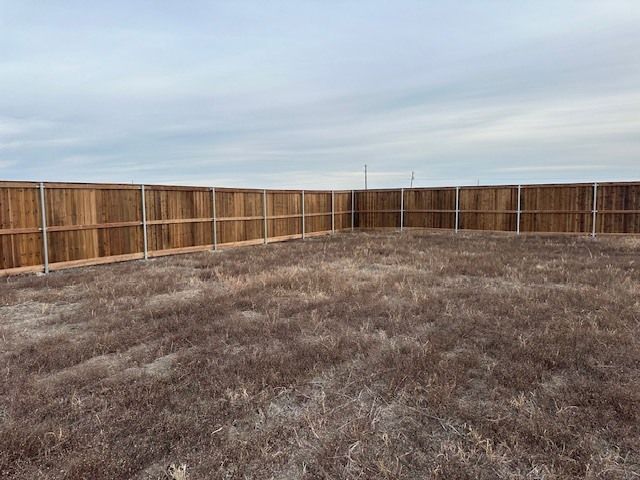 Empty backyard with dry grass and a wooden privacy fence under a cloudy sky