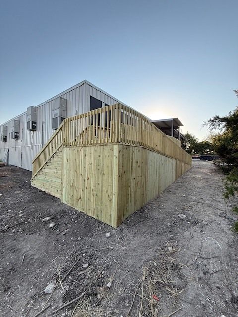 Wooden stair and deck structure attached to a white building on a dirt slope at sunset