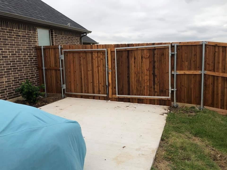 Backyard concrete patio beside brick house and wooden privacy fence, with grass and a covered grill.