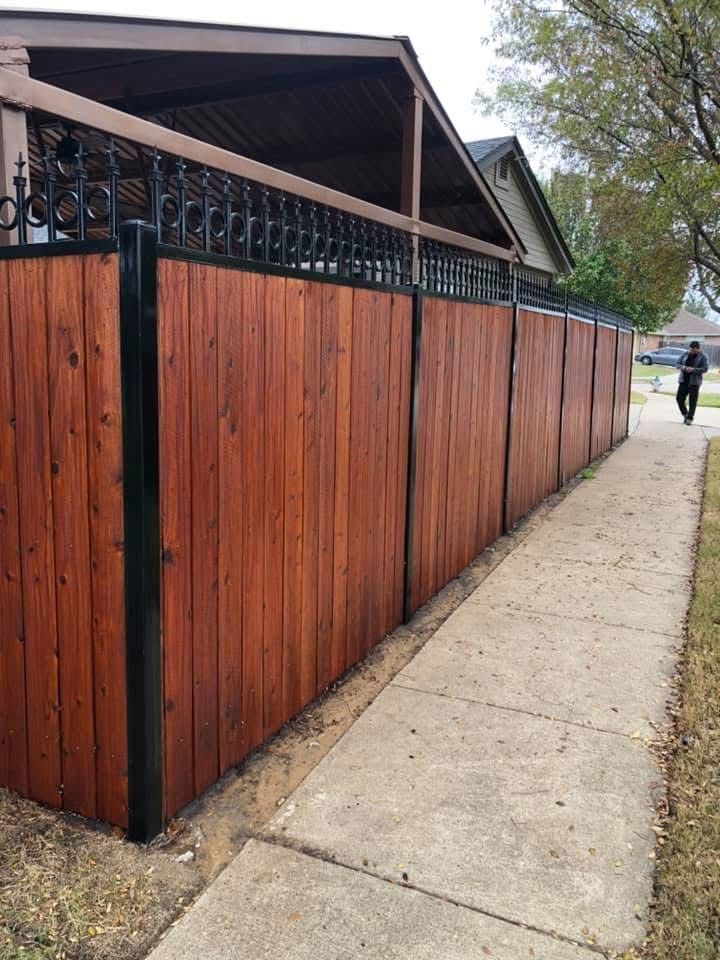 Wooden fence along a sidewalk beside houses, with a person walking in the distance.