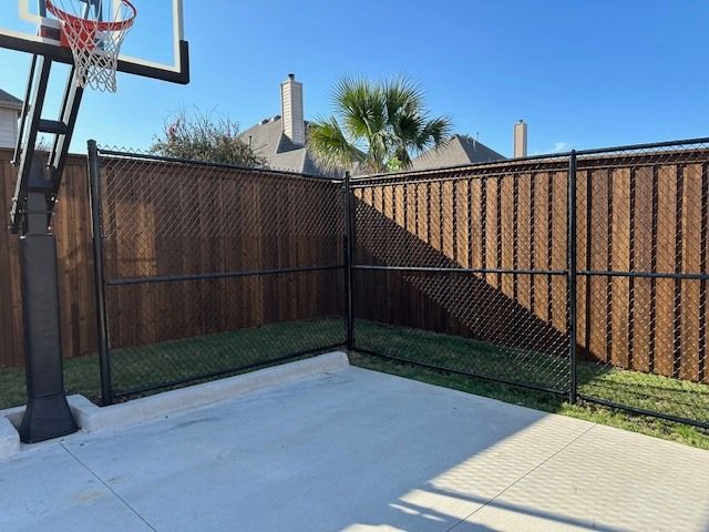 Backyard basketball hoop beside a fenced patio, with a palm tree and clear blue sky