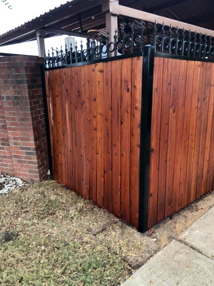 Wooden backyard privacy fence with black metal gate cap beside a brick wall and sidewalk