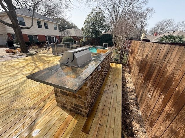 Backyard deck with a brick outdoor grill island beside a fenced patio and pool area