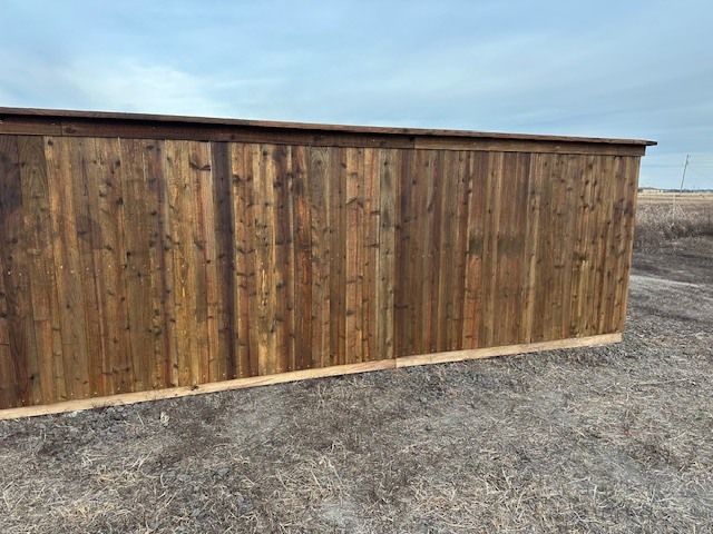Wooden privacy fence with weathered planks along a gravel lot under a clear sky