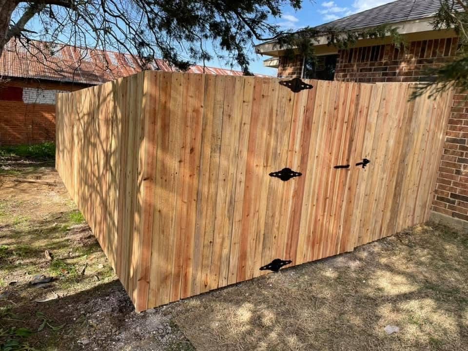 Wooden outdoor storage shed with black hinges and doors, set beside a brick house and trees